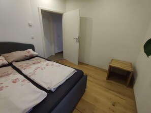 Un dormitori amb un llit, una porta i un petit tamboret de fusta.