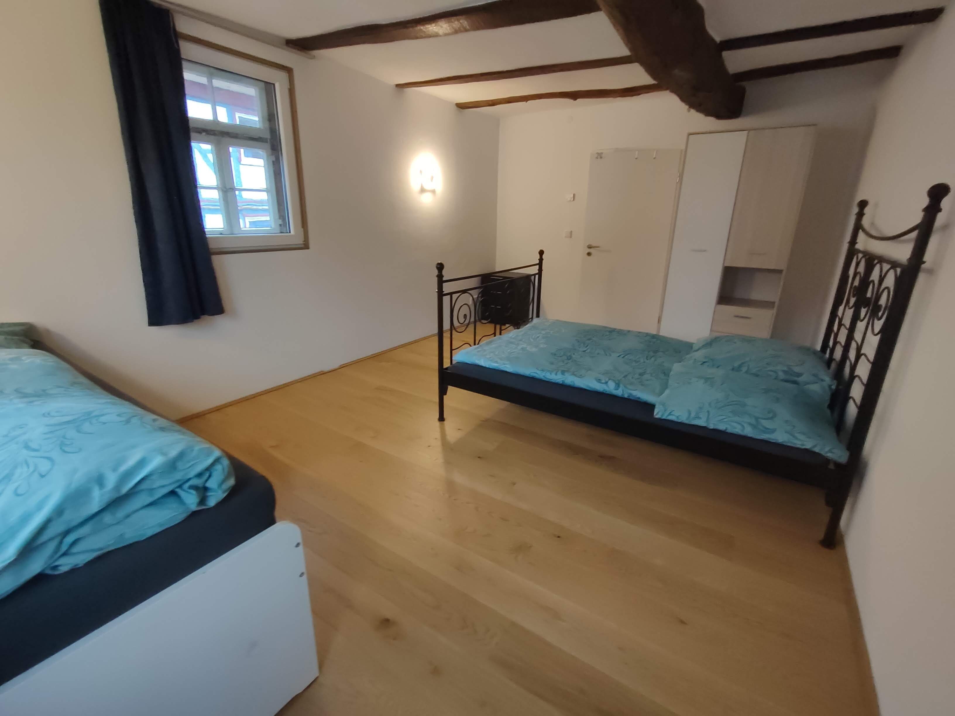 Une chambre avec deux lits, une armoire, une petite table et une fenêtre avec des rideaux.
