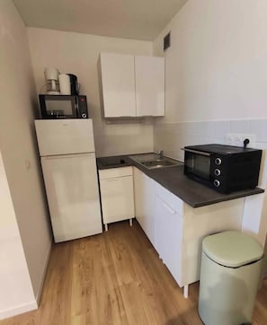 Eine kompakte Küche mit weißen Schränken, einer Mikrowelle, einem Toaster und einem Spülbecken.