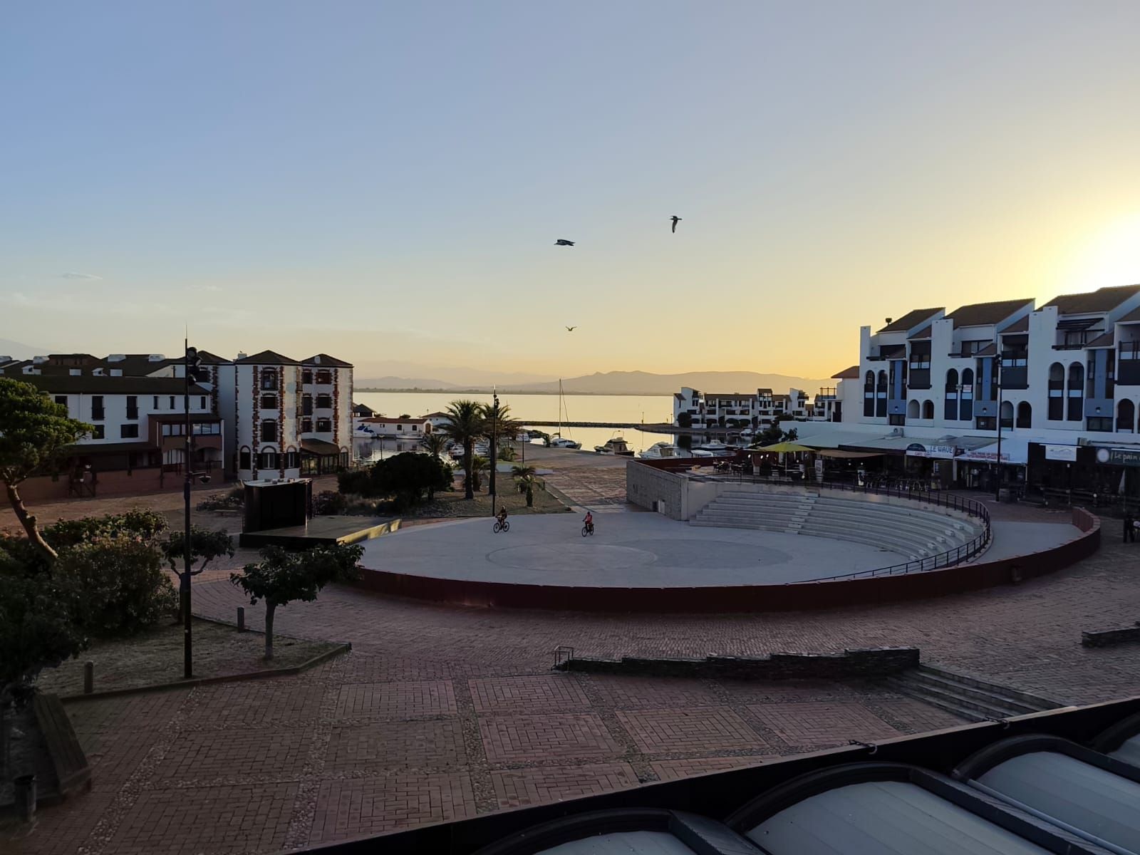 Un paseo marítimo con edificios, un escenario circular y vista al mar.