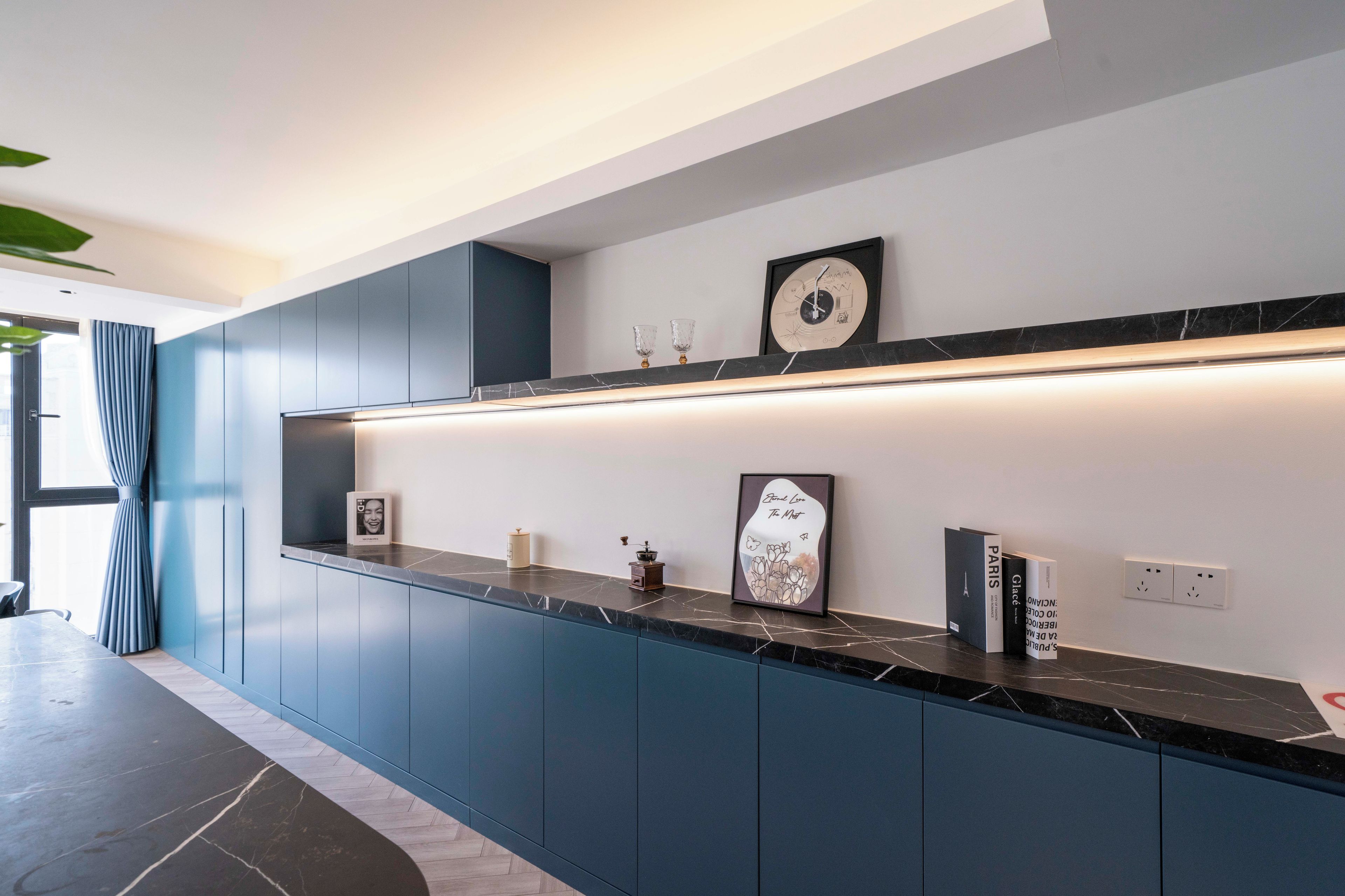 Una cucina moderna con mobili blu scuro, un piano di lavoro in marmo e un orologio a parete.