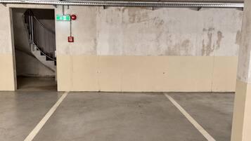Un estacionamiento vacío con pisos de concreto, una señal de salida visible y un detector de incendios.