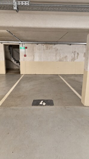 Un estacionamiento vacío con pisos de concreto, una señal de salida visible y un detector de incendios.