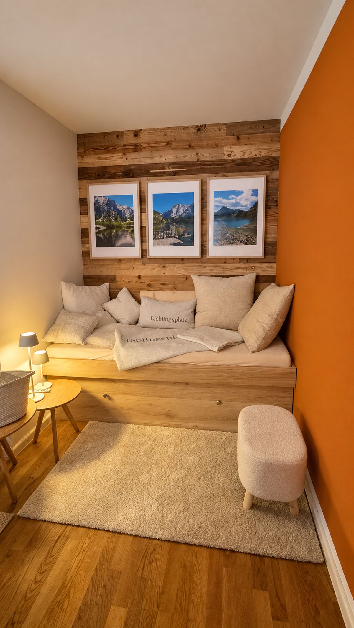 A cozy room with a wooden headboard, a sofa with multiple cushions, a small round table with a lamp, and a rug on the floor.
