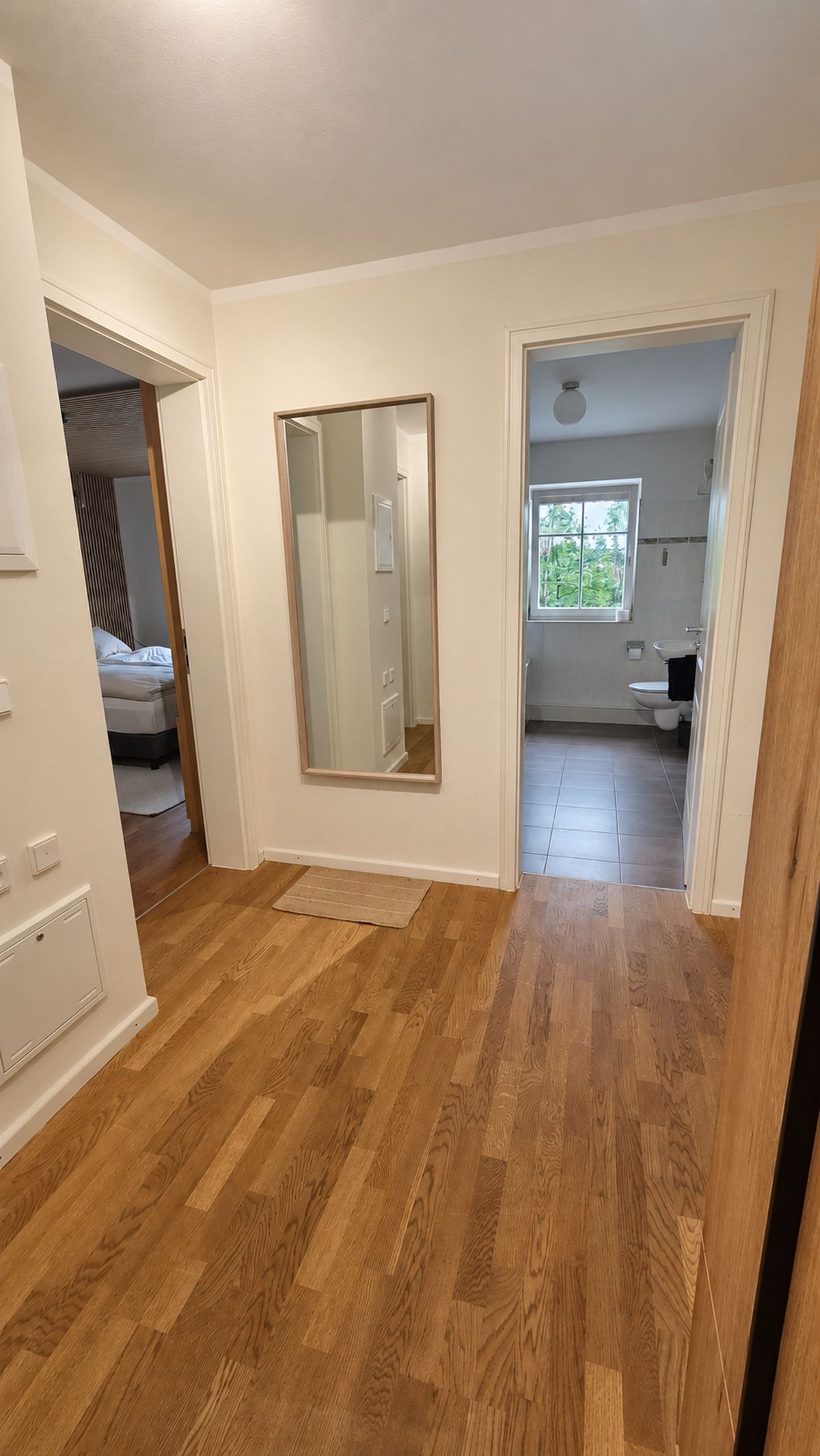 Une pièce spacieuse avec un plancher en bois, un grand miroir et une vue sur une chambre et une salle de bain.