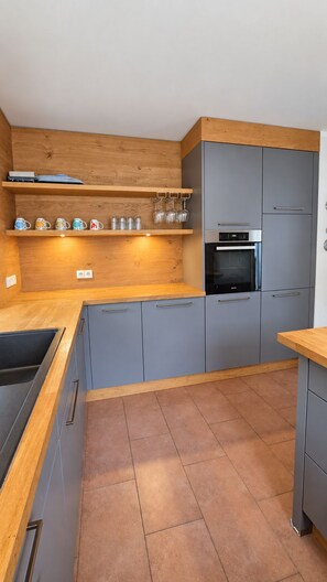 Una cocina moderna con armarios grises, encimeras de madera y un horno empotrado.