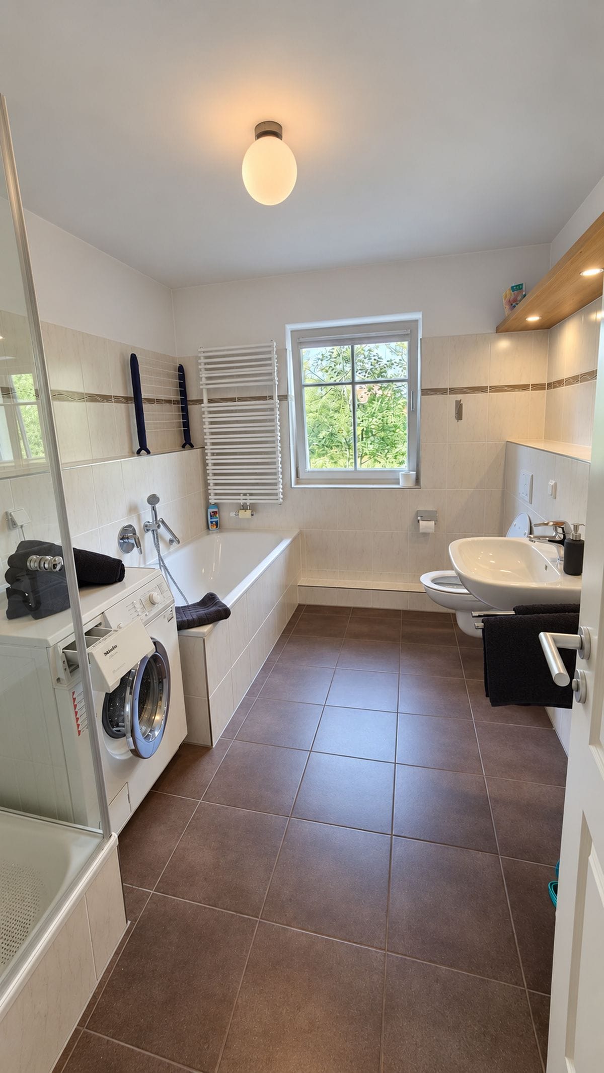 Ein modernes Badezimmer mit Waschmaschine, Badewanne, Toilette und einem Fenster für natürliches Licht.
