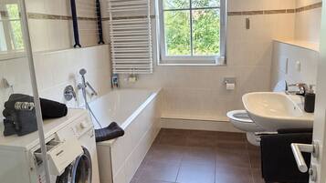 Ein modernes Badezimmer mit Waschmaschine, Badewanne, Toilette und einem Fenster für natürliches Licht.
