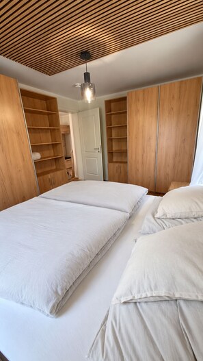 Een slaapkamer met een houten spiltrap plafond, een bed met witte beddengoed en ingebouwde houten kasten.