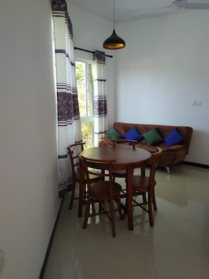 A dining area with a round table and chairs, a sofa with cushions, and a hanging pendant light. - Denzil House: Accommodation for 3 People (Ahangama)