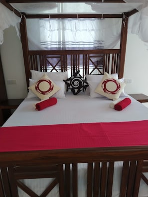 Uma cama com dossel, almofadas com padrão circular e colcha vermelha.