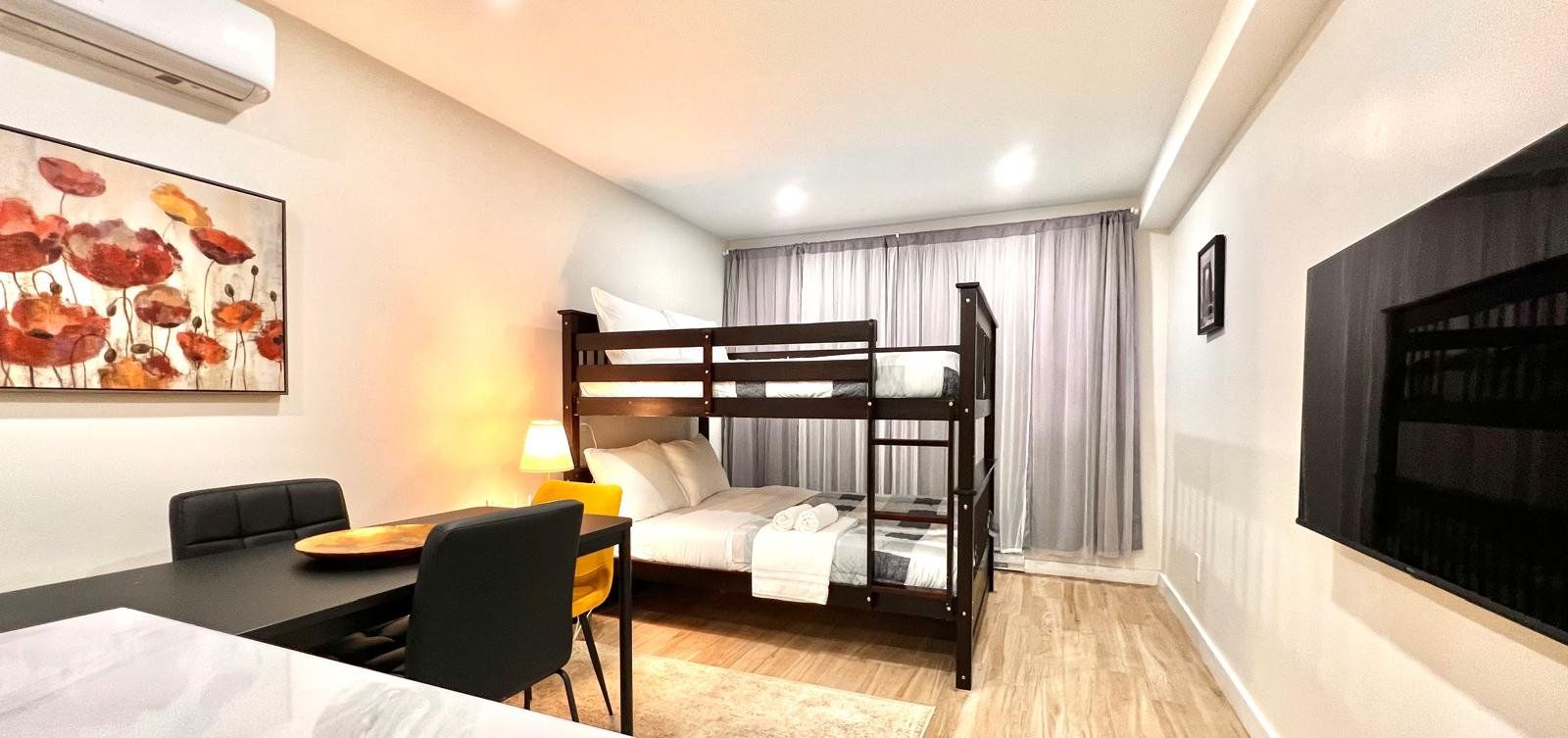 Habitación de hotel con literas, un escritorio con silla, una lámpara y un cuadro en la pared.