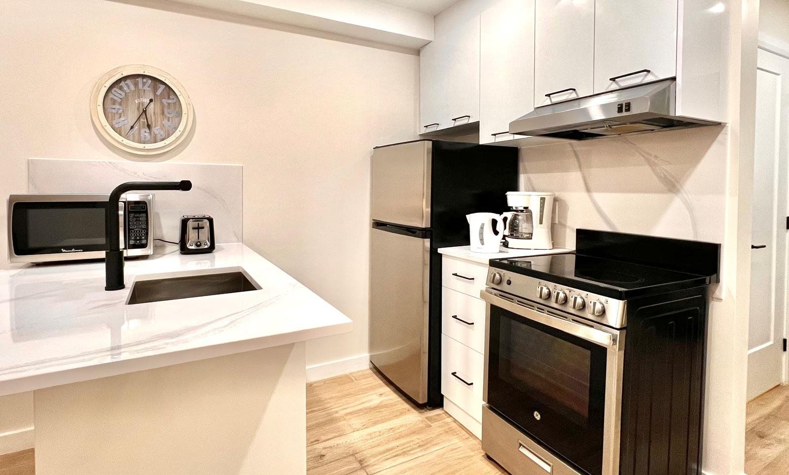 Una cocina moderna con encimera blanca, microondas integrado, cafetera, estufa y refrigerador.