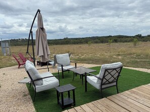 Ein Sitzbereich im Freien mit Tisch und Stühlen, einer Schaukel und Blick auf ein Wiesenfeld.