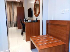 Quarto de hotel com cama de madeira, uma escrivaninha com cadeira, televisão e espelho.