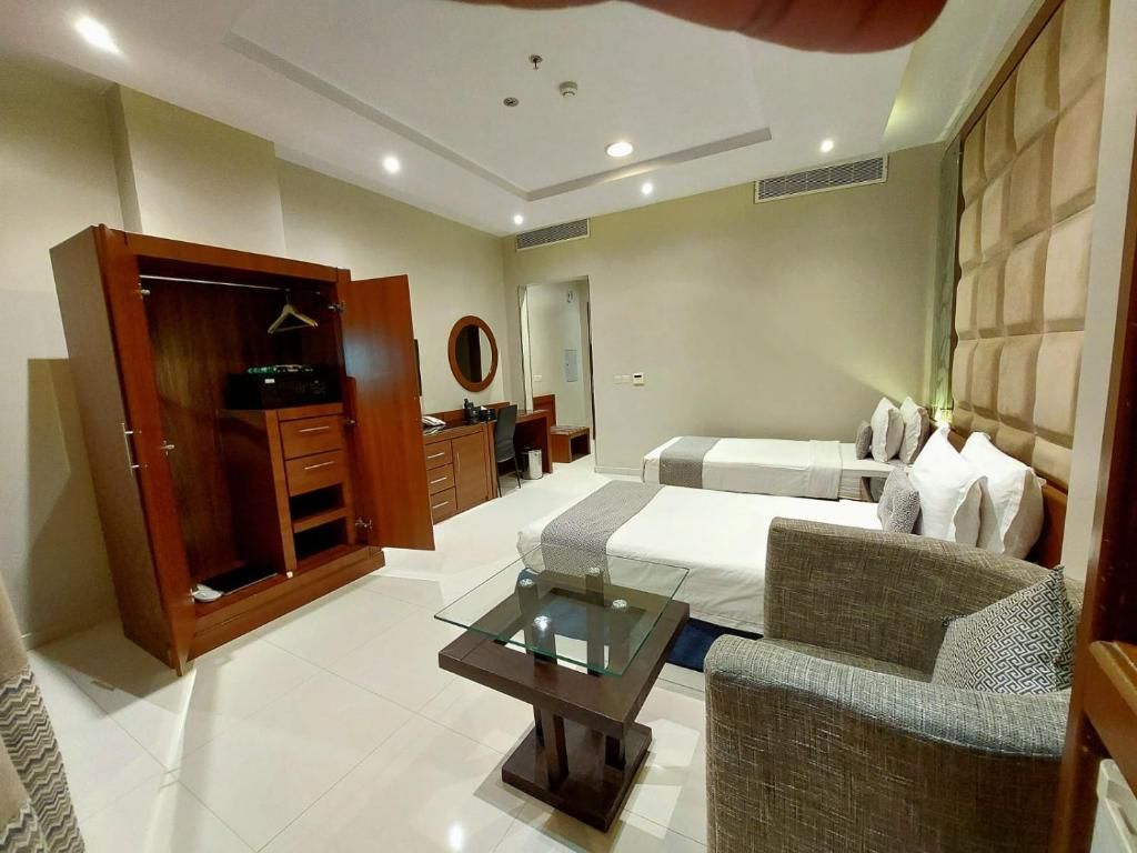 A hotel room with a bed, a sofa, a glass-top coffee table, a wardrobe, and a mirror.