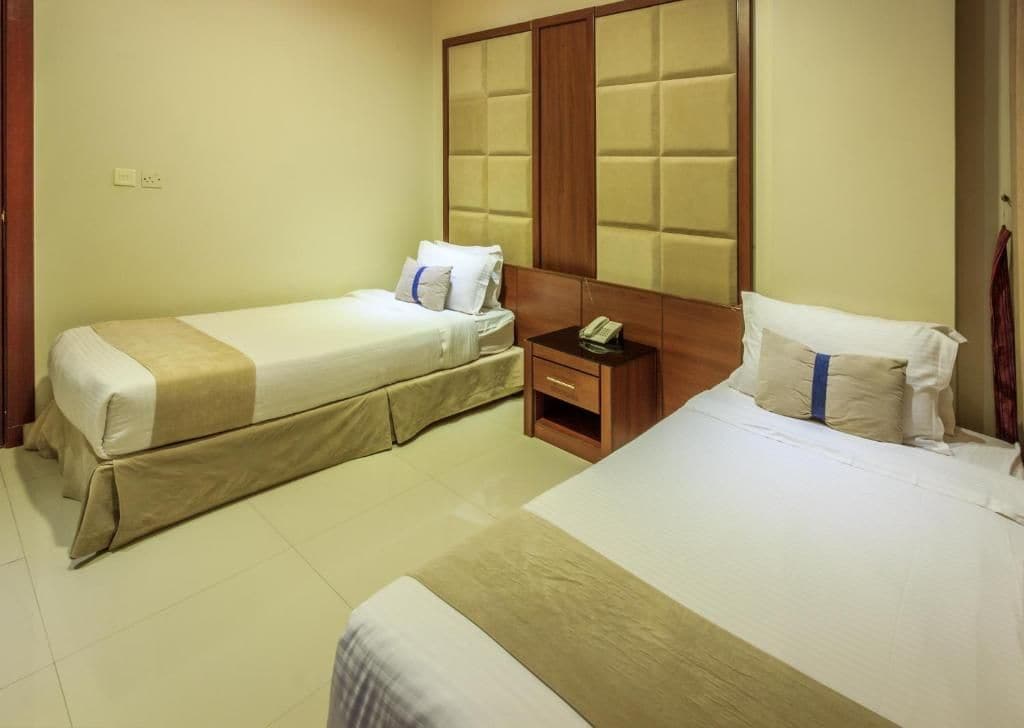 A hotel room with two single beds, a wooden headboard, a bedside table with a phone, and a small nightstand.