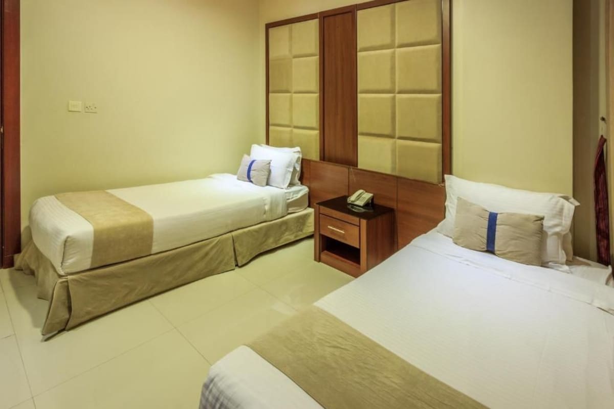A hotel room with two single beds, a wooden headboard, a bedside table with a phone, and a small nightstand.