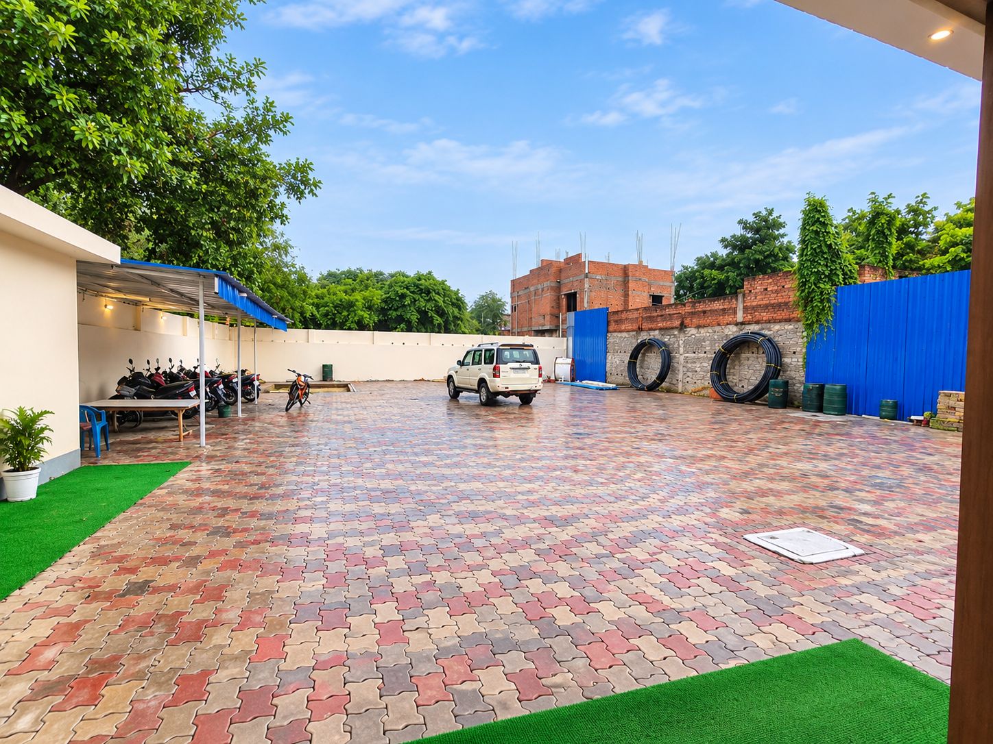 A paved courtyard with a vehicle, parked motorcycles, and a blue fence.