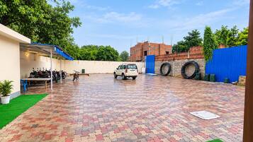 A paved courtyard with a vehicle, parked motorcycles, and a blue fence.