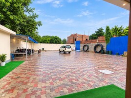 A paved courtyard with a vehicle, parked motorcycles, and a blue fence.