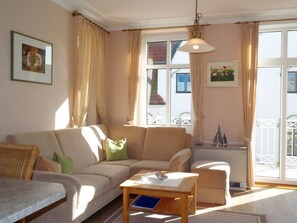 A living room with a sofa, a small table, and a window with curtains. - Haus Hansen Wyk - Holiday Apartment 02 (Wyk auf Foehr)