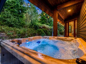 Een hottub met een houten buitenkant, omgeven door weelderige begroeiing en een houten terras.