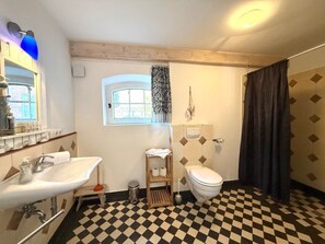 A bathroom with a checkered floor, a sink, a toilet, and a window with curtains. - Holiday Home in Oldsum With Swimming Pool (Oldsum)