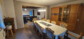 A dining area with a long table, chairs, and a cabinet with glass doors. - Vacation Home "Im alten Kiosk" - Relaxation Right on Lake Idasee (Ostrhauderfehn)