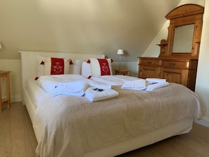 A neatly made bed with white linens and red decorative pillows, a wooden dresser, and a mirror. - 5 in the Deichhof House (Dunsum)