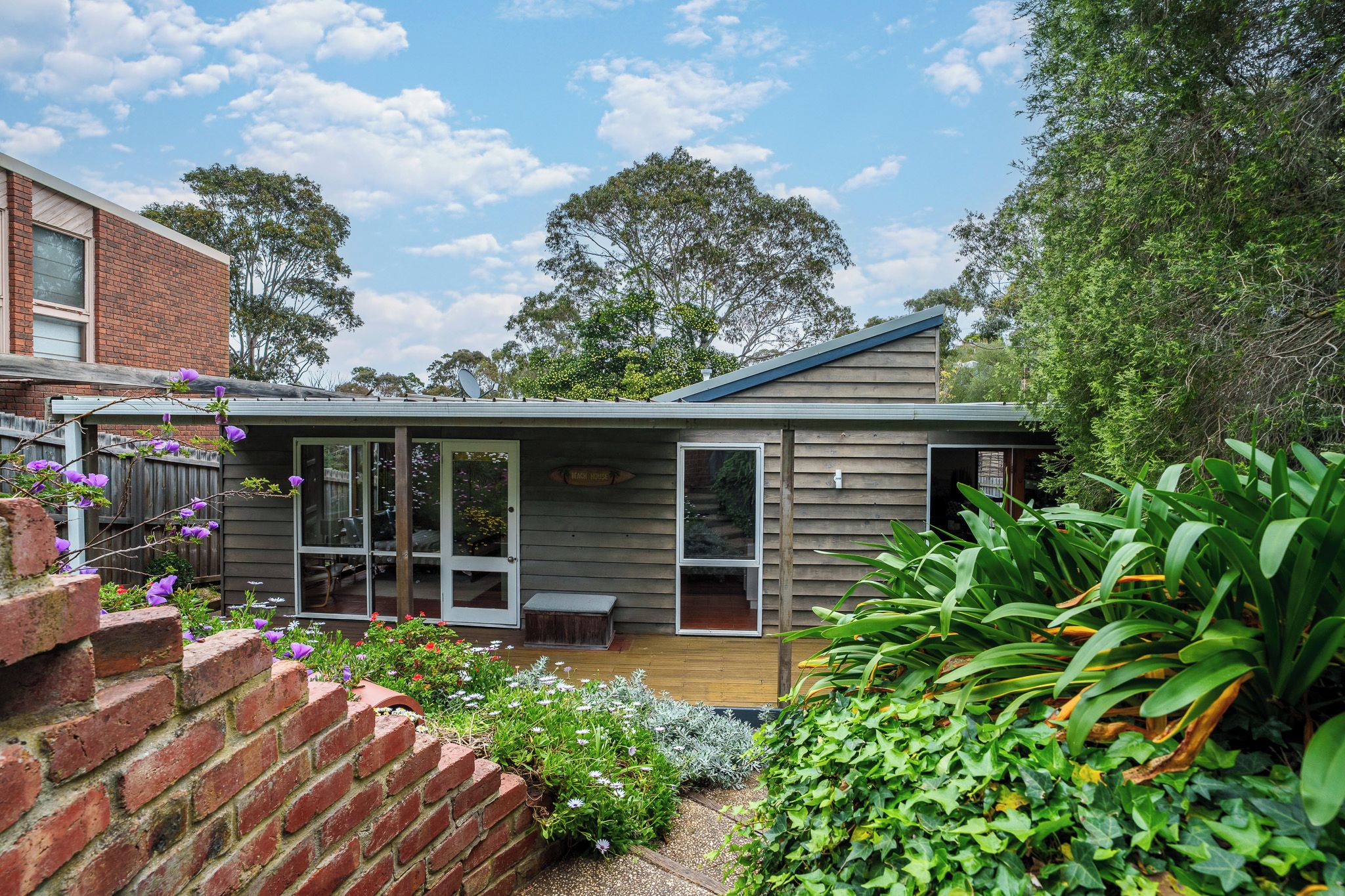 A modern house with a deck, surrounded by lush greenery and a clear sky.