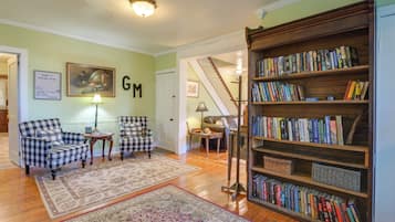 Un salon avec des fauteuils à motifs à carreaux, une bibliothèque, un tableau et un tapis.