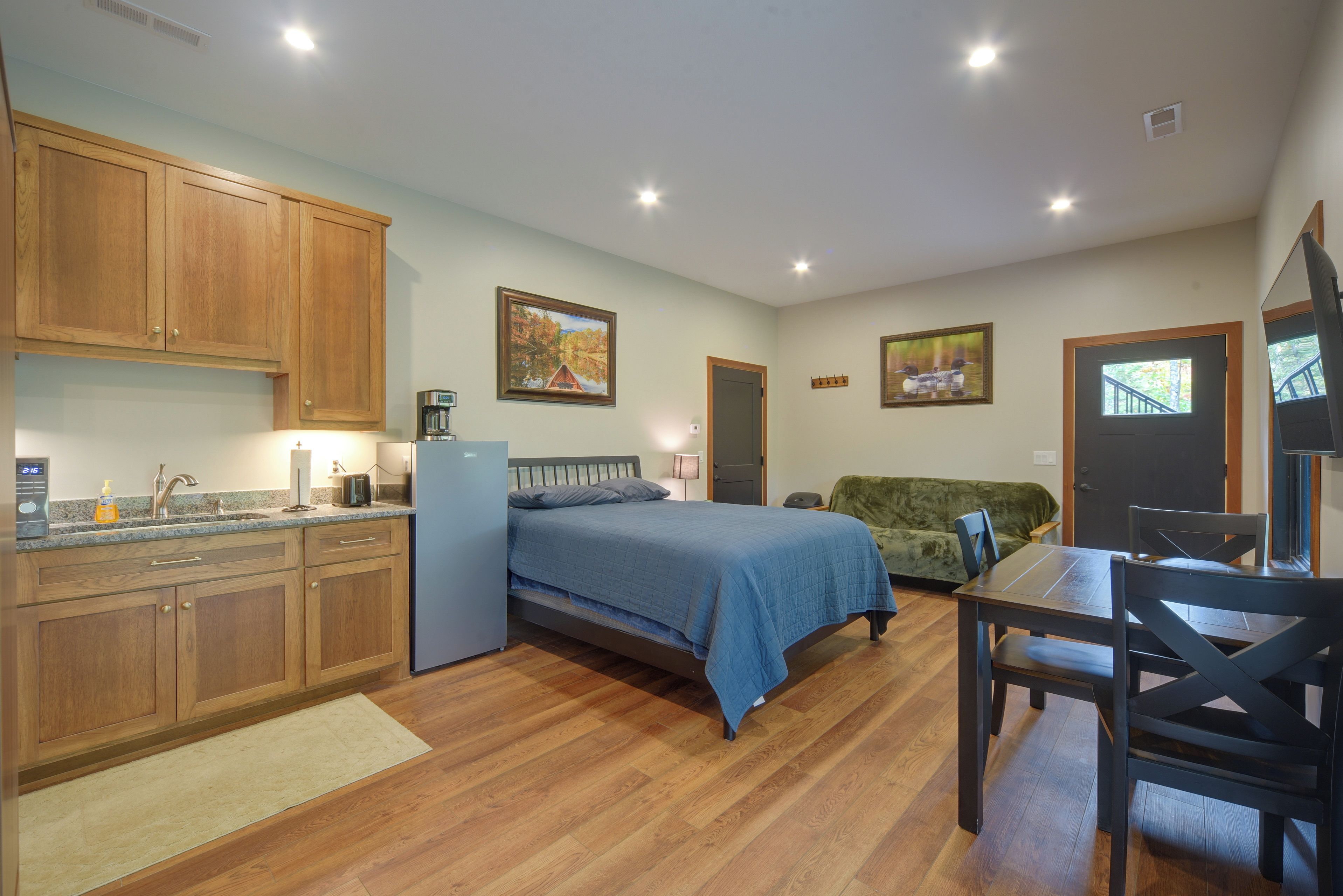 A compact room with a bed, a small kitchenette, a dining area, and a door leading to another room.