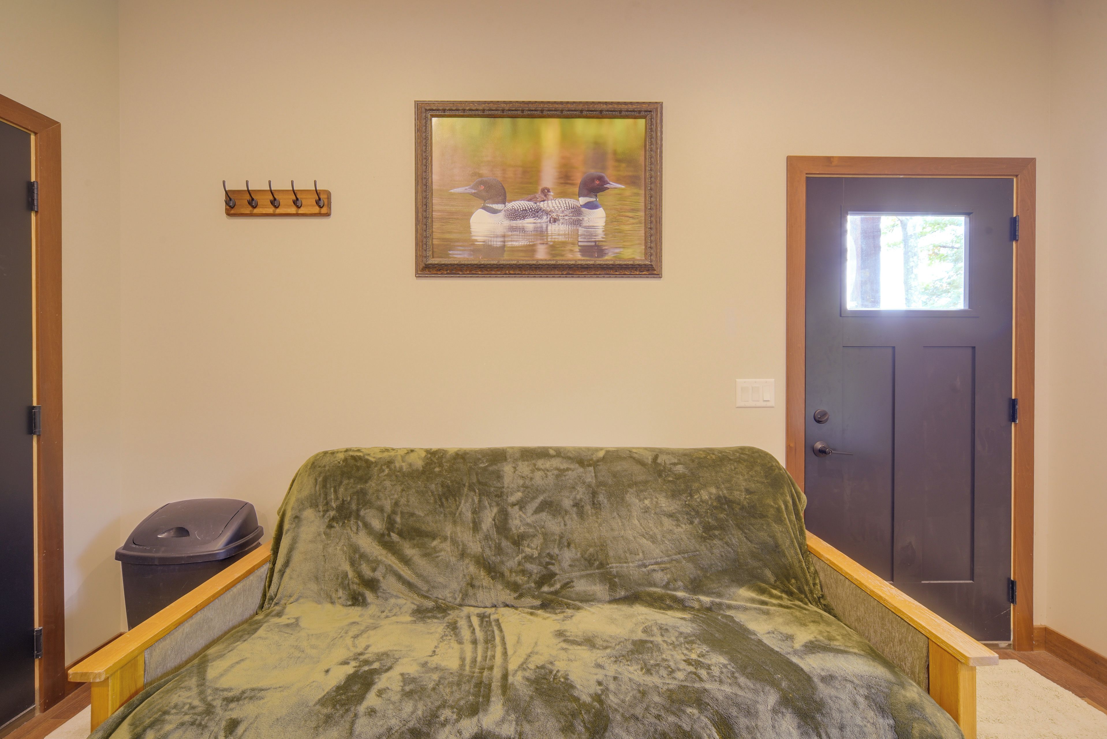 A room with a green sofa, a door, a coat rack, and a framed picture on the wall.