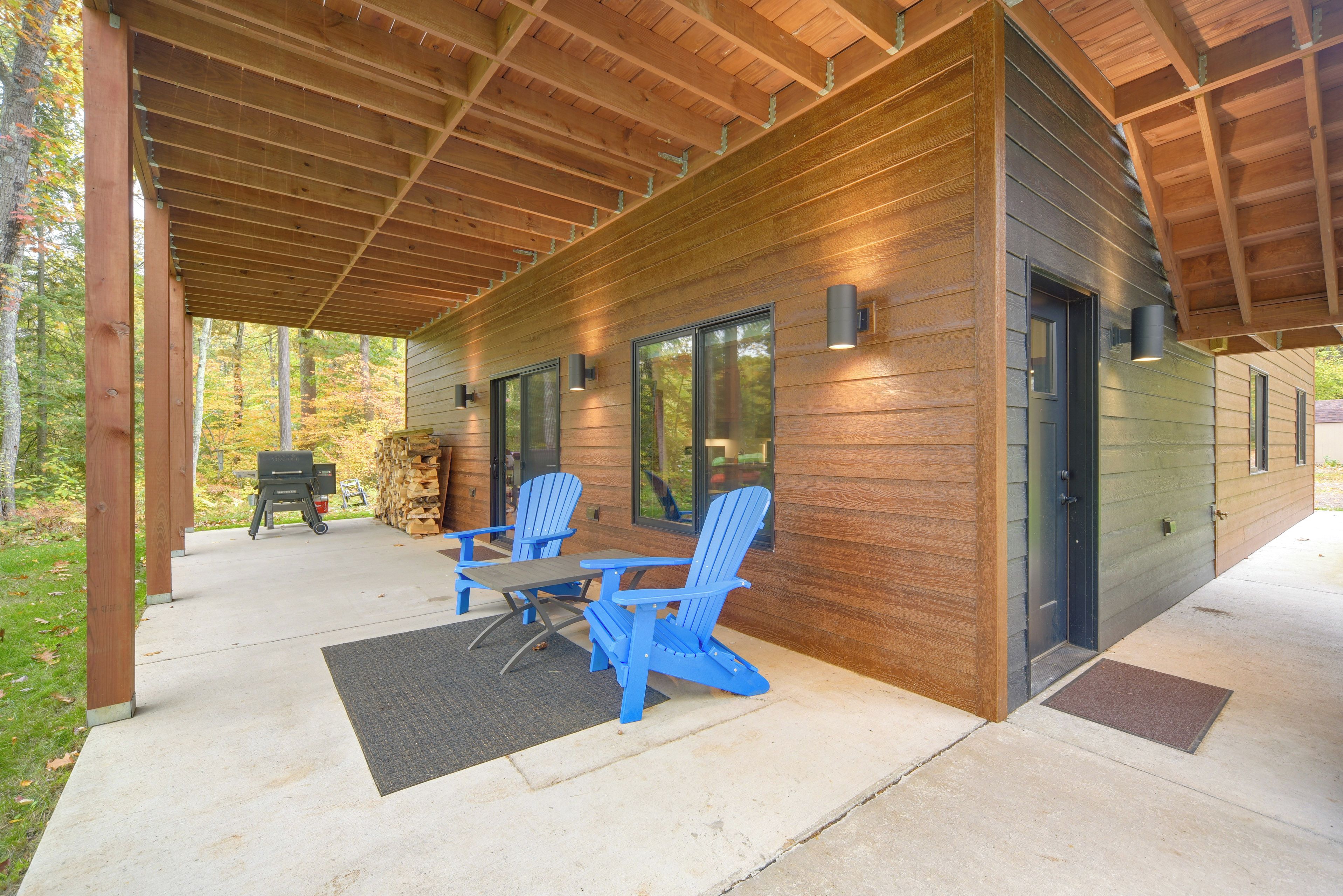 A covered outdoor area with a table and chairs, a grill, and a stack of firewood.