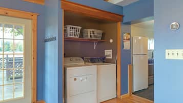 A laundry room with a washing machine, dryer, and stacked laundry baskets on a shelf.