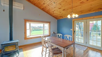 Una habitación con techo de madera, un ventanal grande, una mesa de comedor con sillas y un estufa de leña.