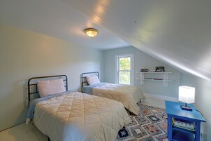 Un dormitorio con dos camas, una ventana, una estantería con libros y un escritorio con una lámpara.
