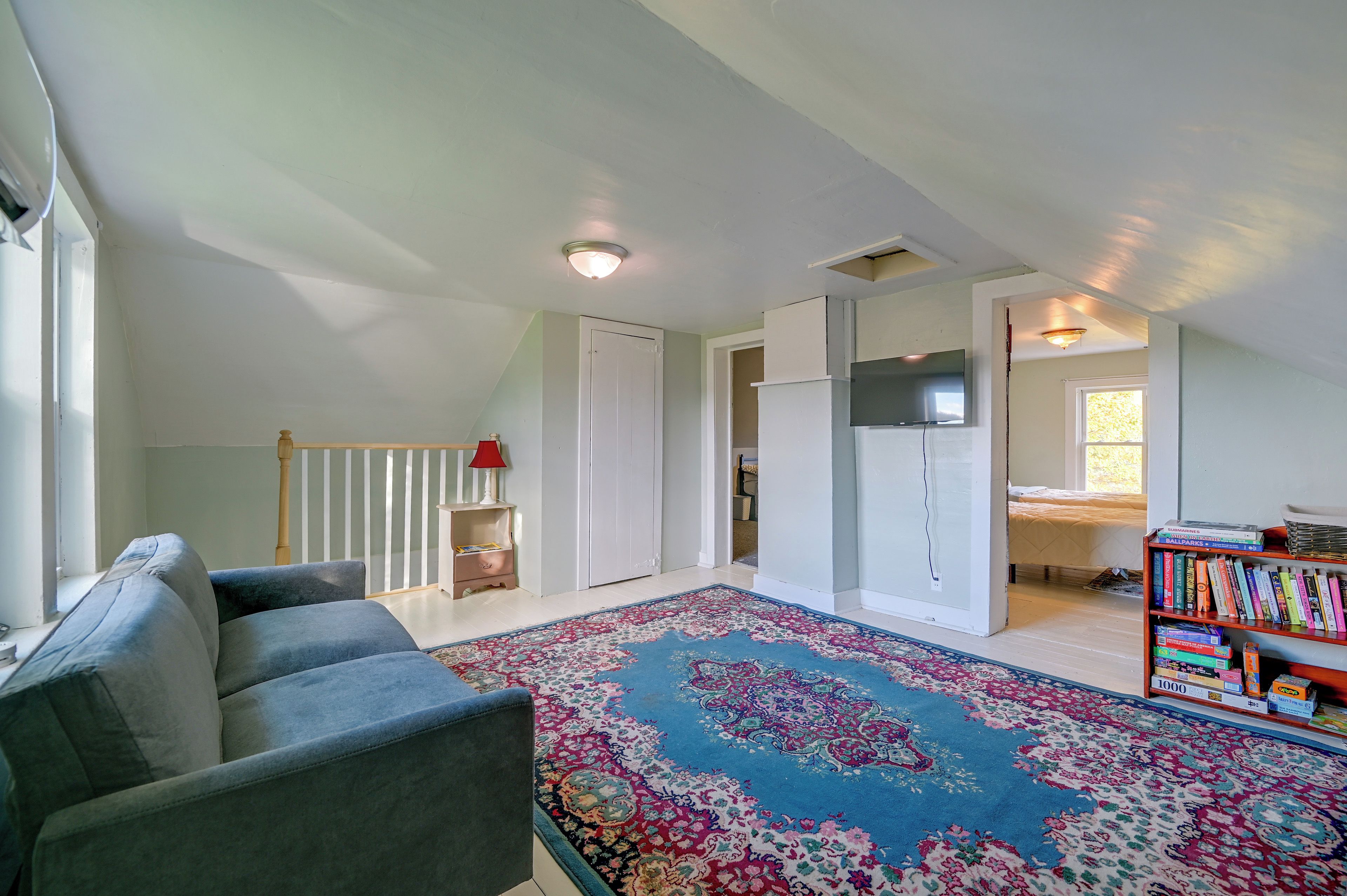 A spacious living room with a sofa, a patterned rug, a bookshelf, and a door leading to another room.
