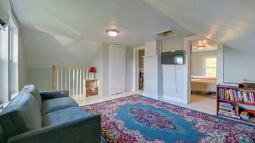 A spacious living room with a sofa, a patterned rug, a bookshelf, and a door leading to another room.