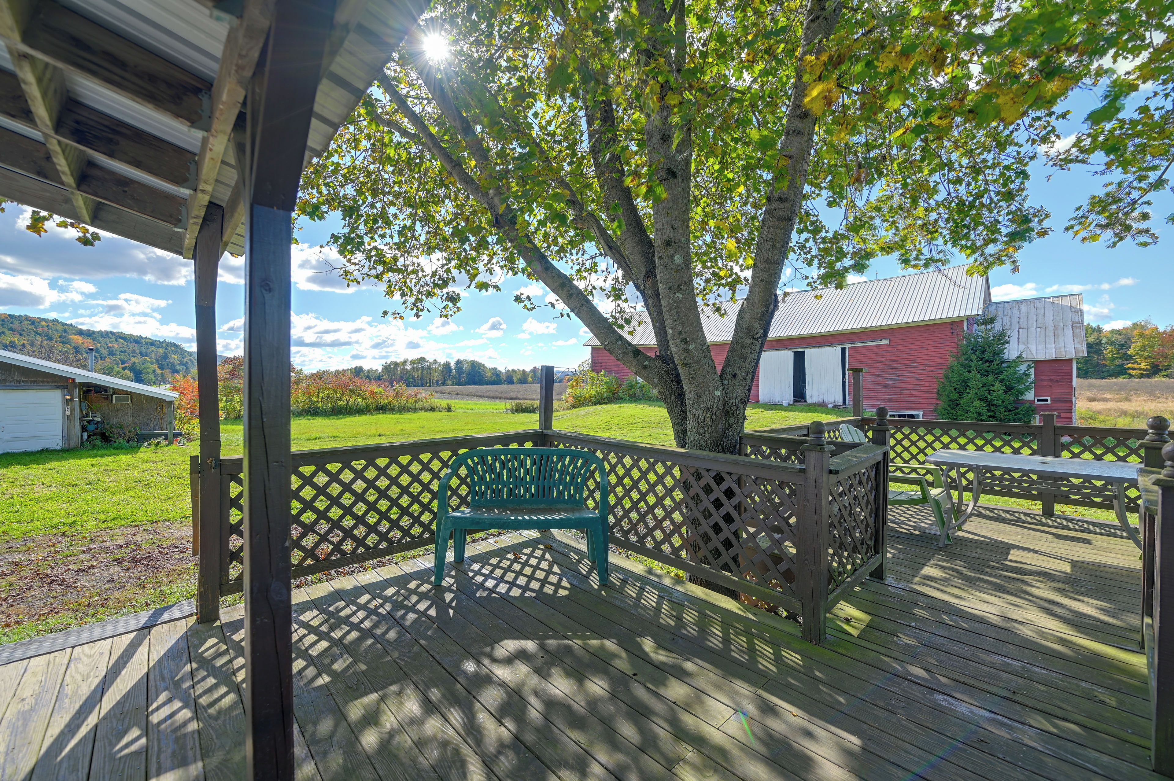 A wooden deck with a bench, a lattice fence, and a view of a red barn and green field.