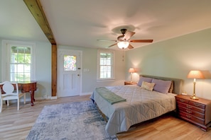 A bedroom with a bed, two bedside tables with lamps, a chair, a wooden desk, a stained glass door, and a ceiling fan.