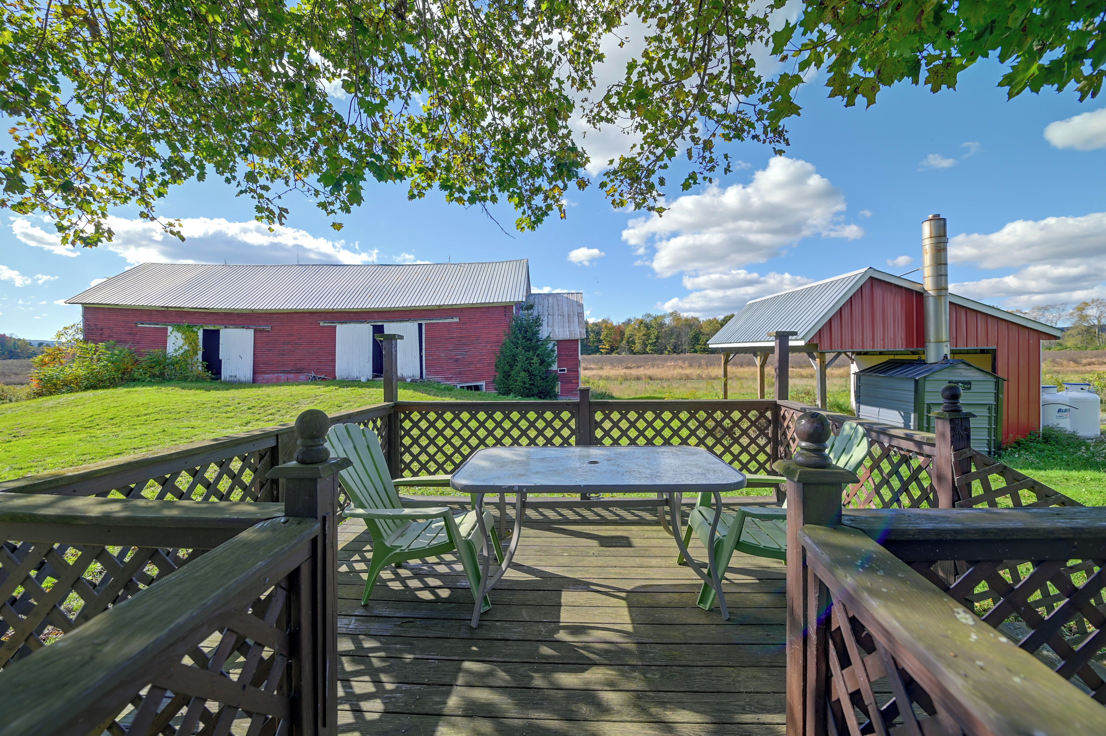 A wooden deck with a table and chairs, a red barn, and a silo in a rural setting.