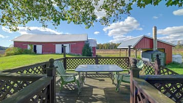 A wooden deck with a table and chairs, a red barn, and a silo in a rural setting.