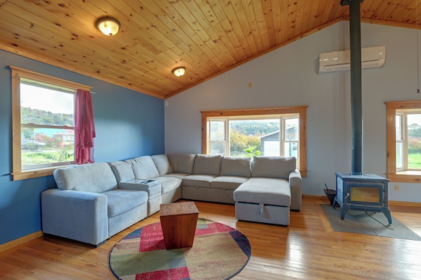 A cozy living room with a sectional sofa, a wooden ceiling, and a wood-burning stove.
