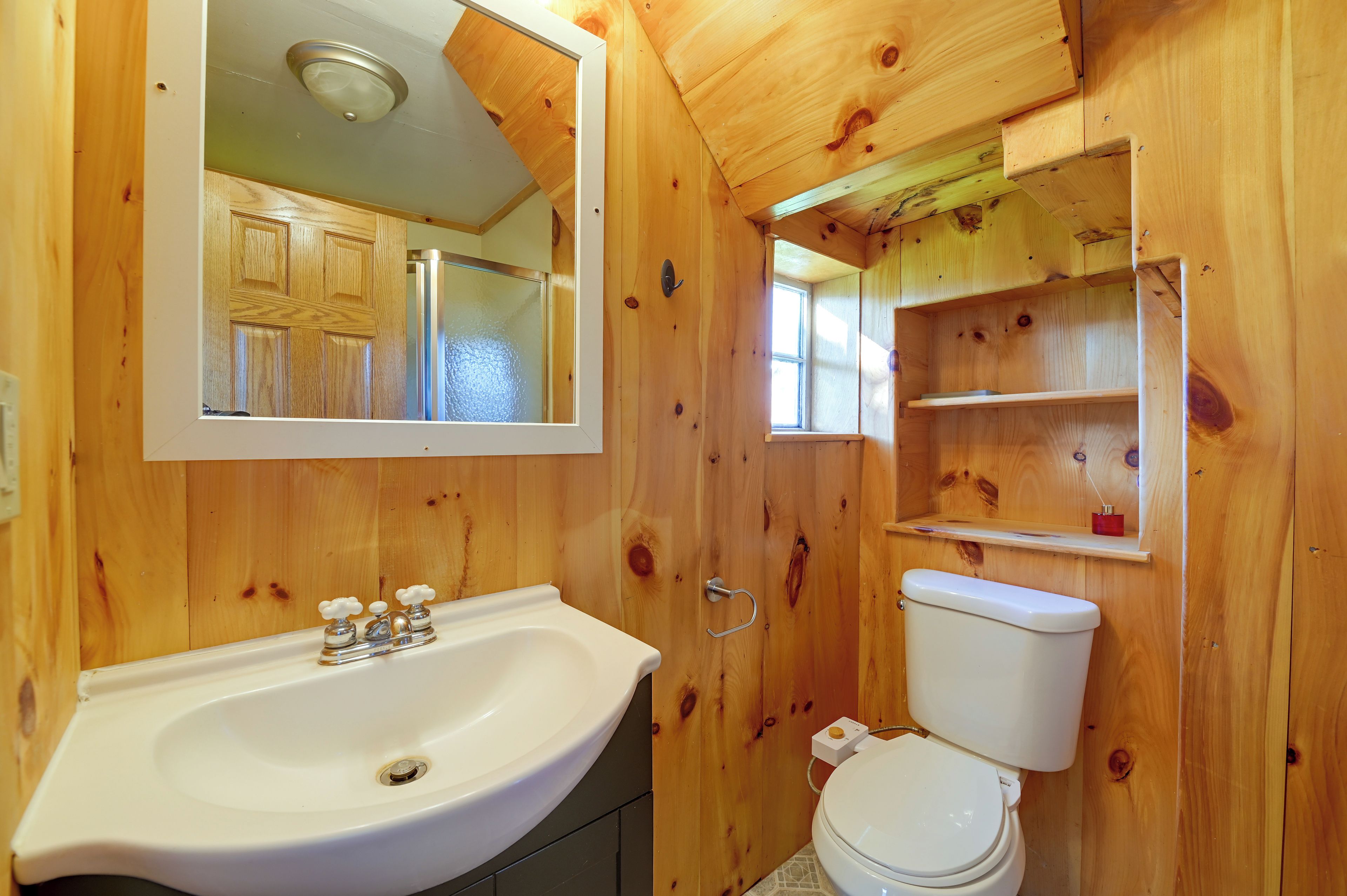 A wooden bathroom with a sink, toilet, and a mirror.