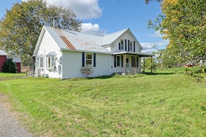 A two-story white house with a metal roof, a porch, and a small garden area.