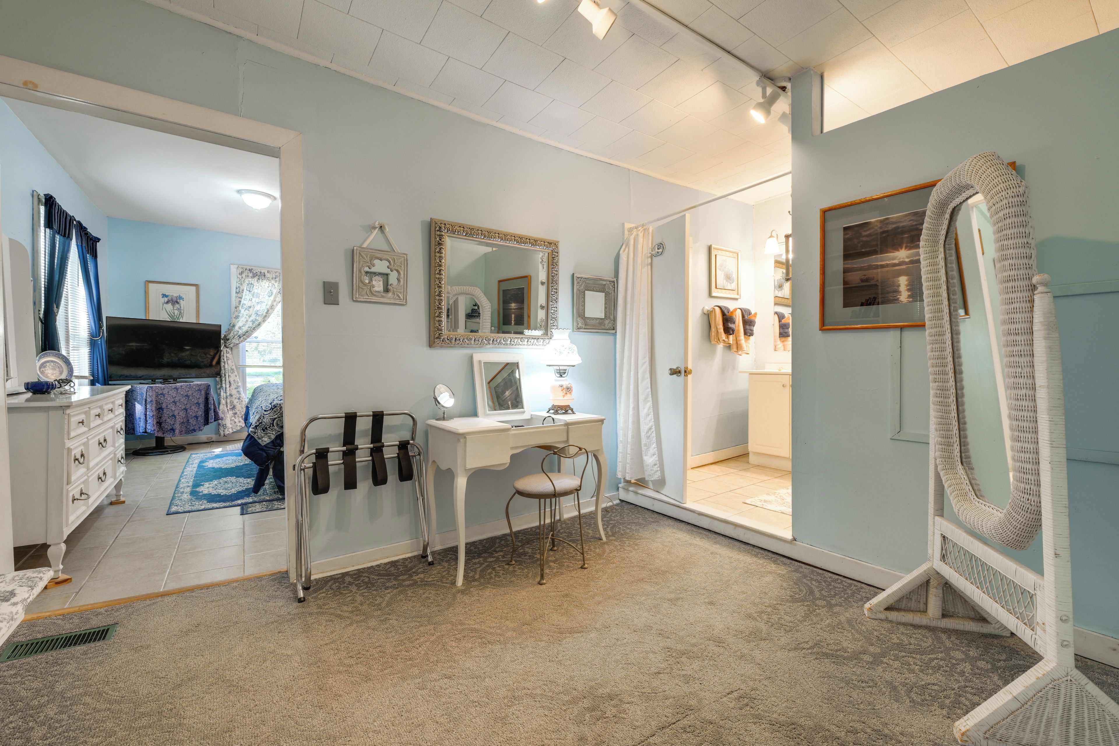 A room with a white vanity, a large mirror, a chair, and a door leading to another room.