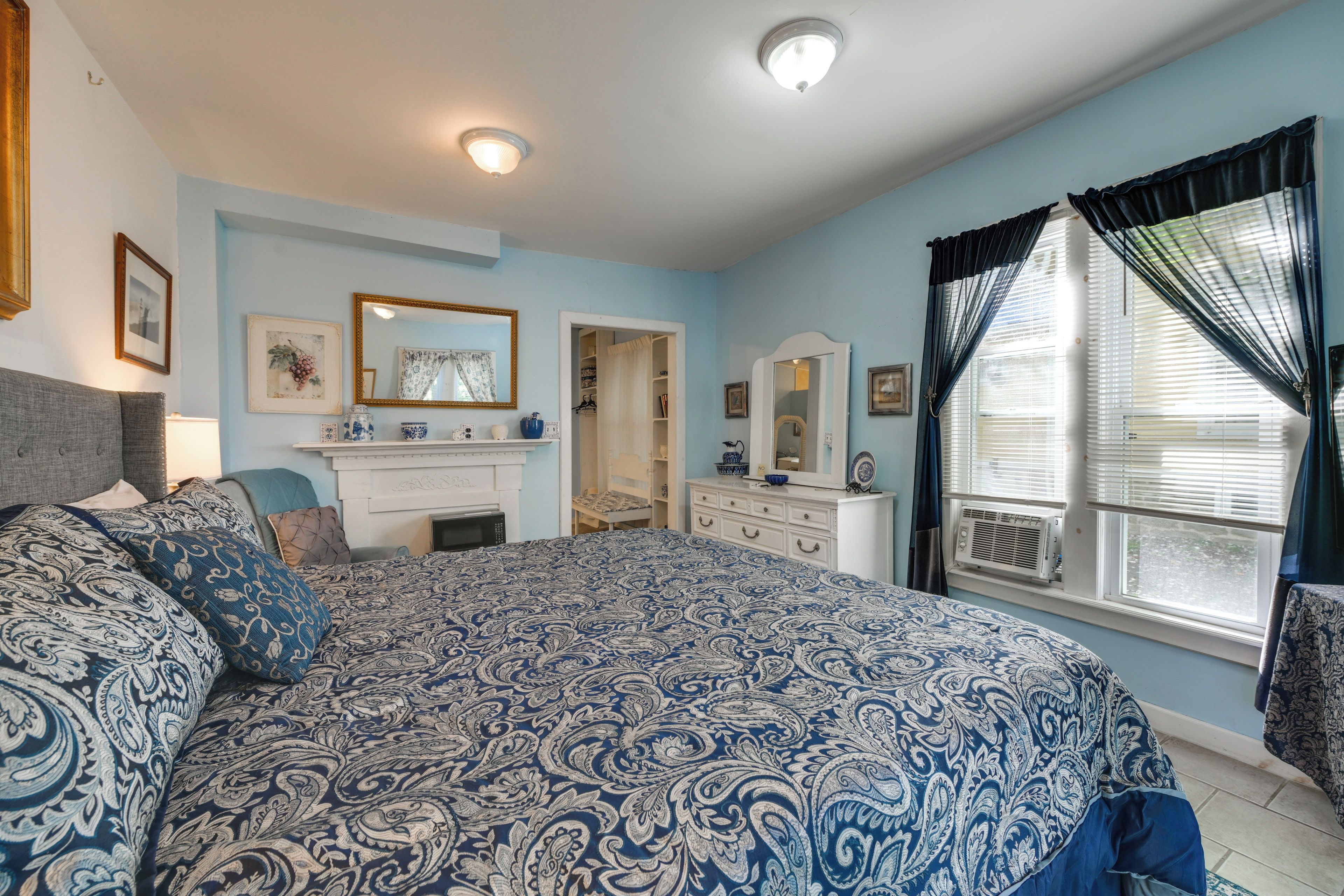A bedroom with a large bed, dresser, and a window with curtains.