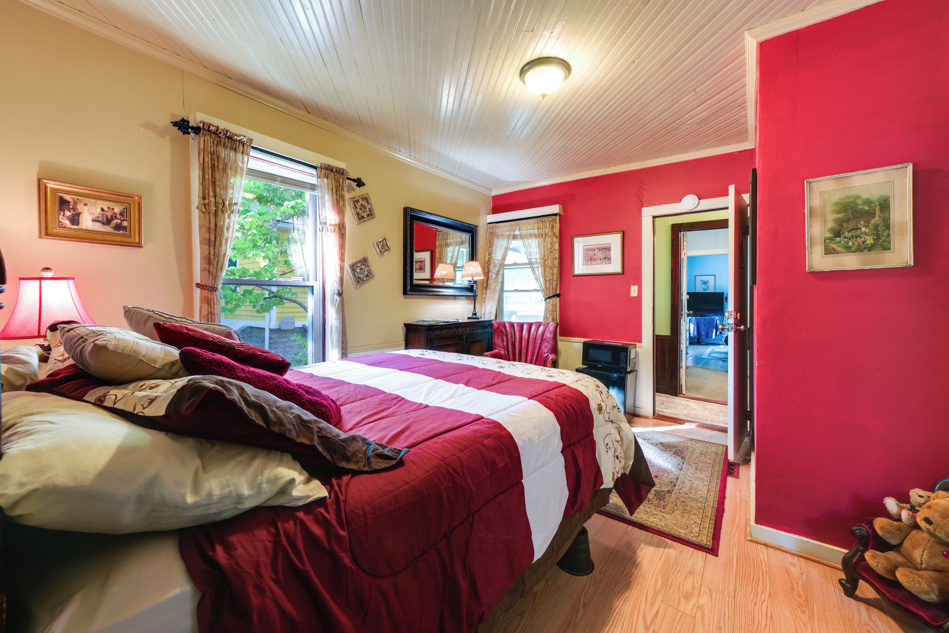 A bedroom with a large bed, a dresser, a mirror, and a door leading to another room.